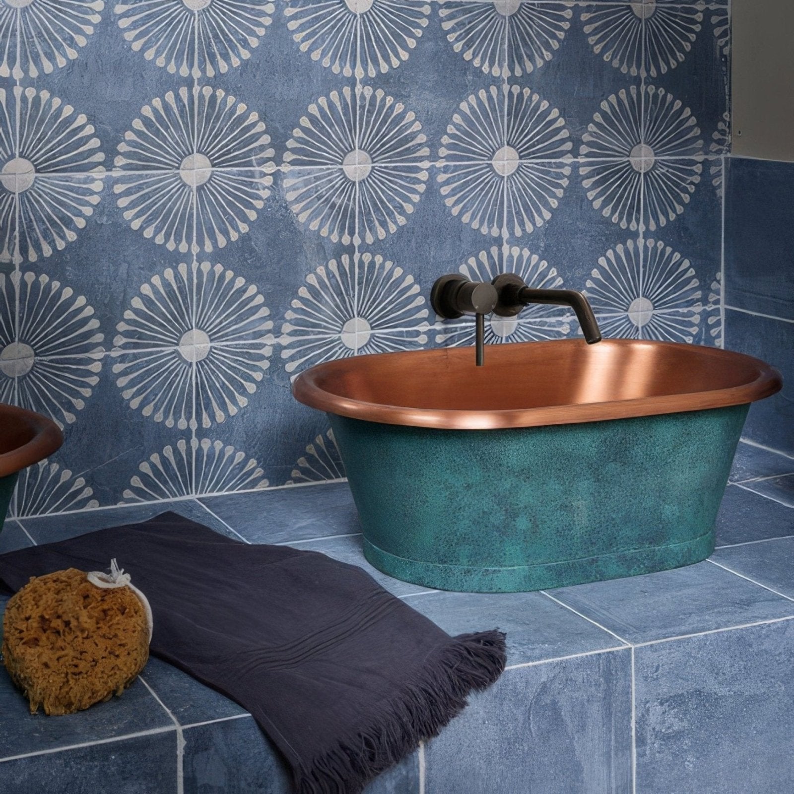 A copper oval bathtub with verdigris patina and a matte black wall-mounted faucet from cuba porcelain indigo field
