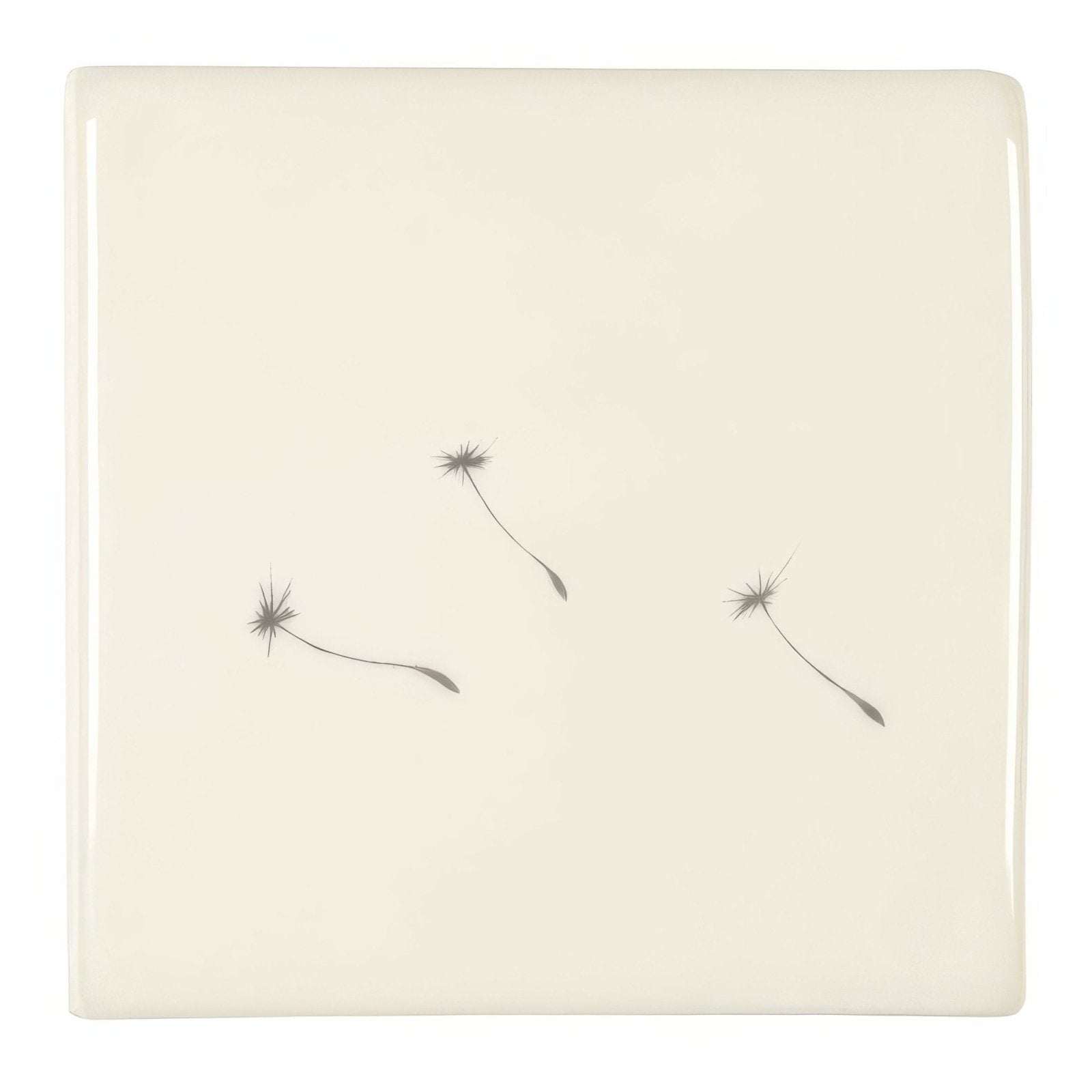 Cream-colored ceramic coaster with minimalist design featuring three delicate gray dandelion seeds floating across surface