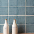 Two cream-colored ceramic bottles with cork stoppers labeled olive oil and vinegar against field tile danube blue tiles