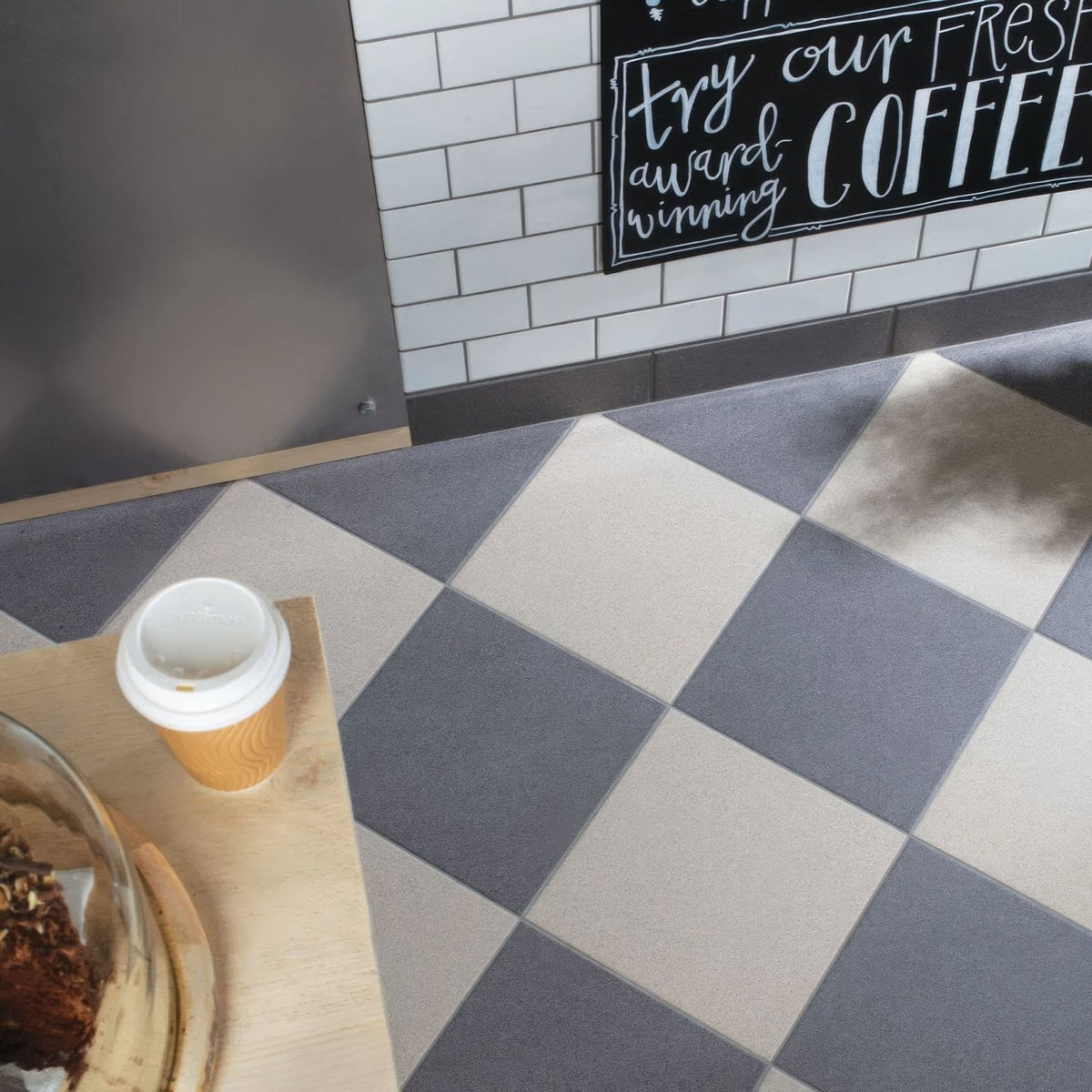 A disposable coffee cup with an orange sleeve on a dark grey flat quarry tile 300x300x9mm wooden surface