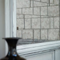 A dark glossy glass vase with a flared top and narrow base in front of a deco glass pewter wall tile