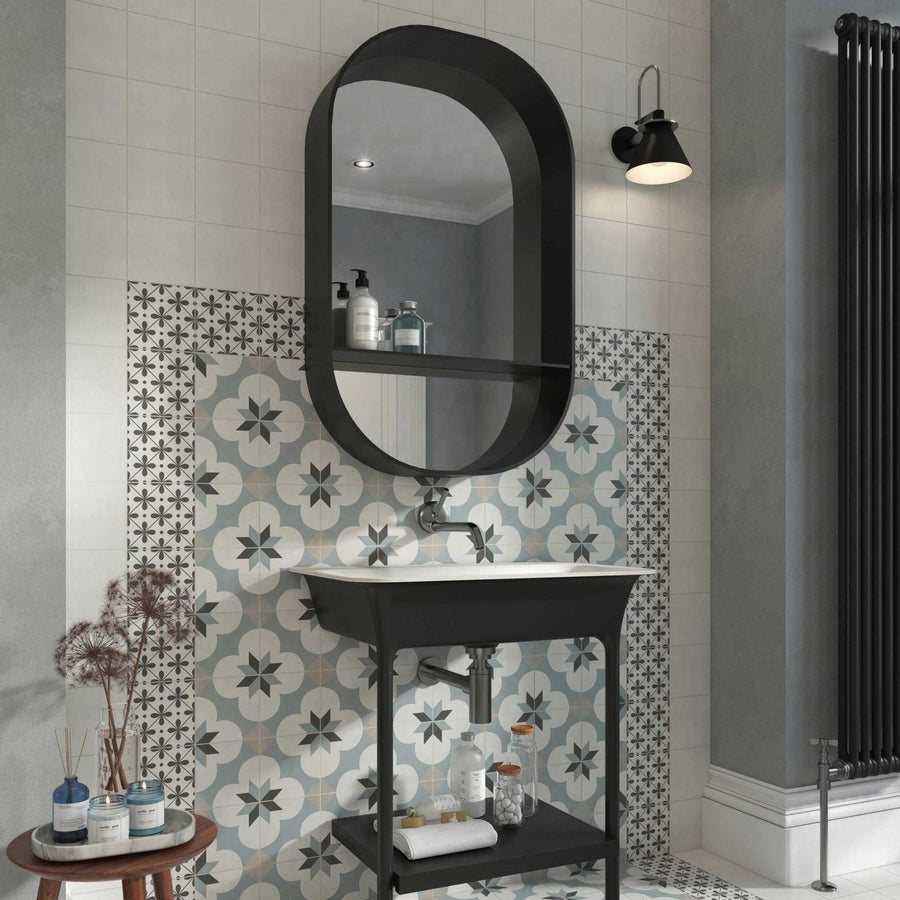 Black oval mirror with integrated shelf above white sink and black vanity base featuring decorata 09 patterned tile