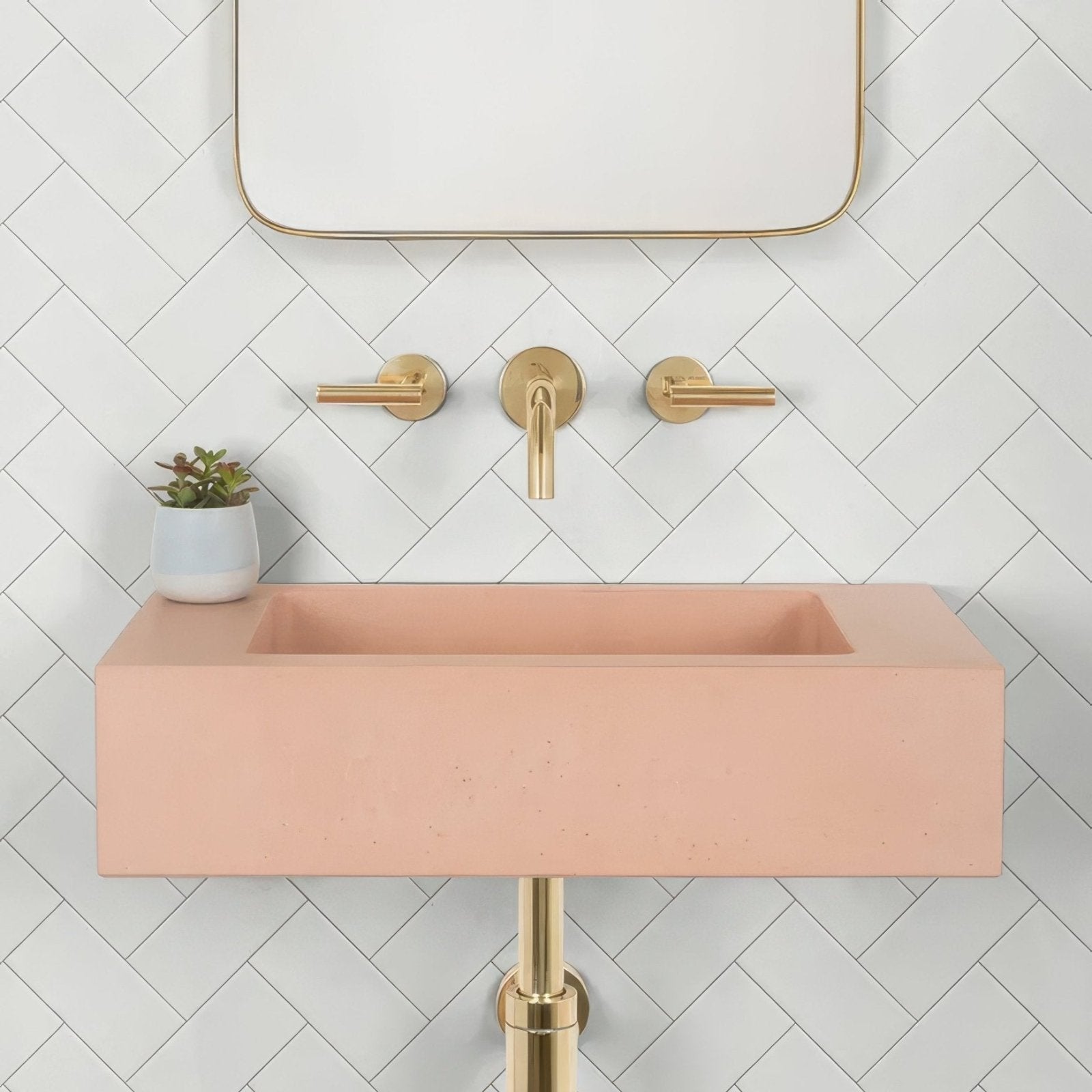 A delicate wall ceramic metro sink with a sleek blush pink concrete body and gold-toned minimalist faucet fixtures