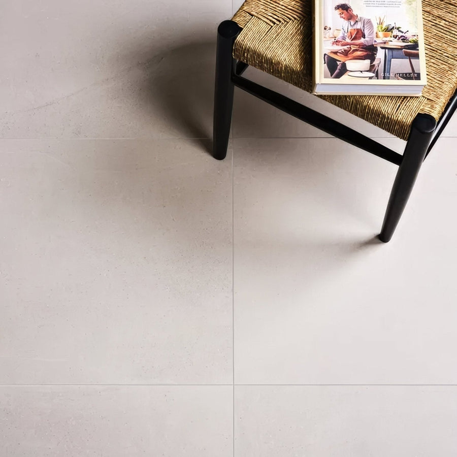 A minimalist black-framed woven chair with natural fiber seat on Dorset Porcelain White floor tiles