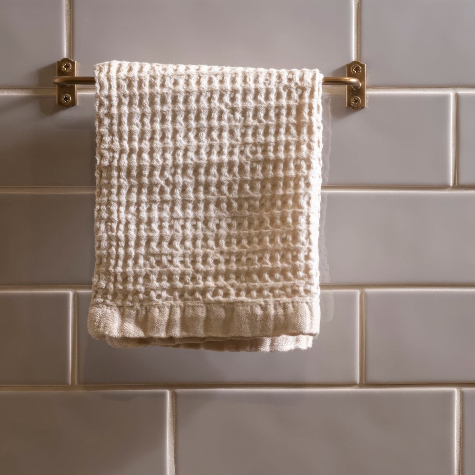 A cream-colored waffle-weave Brick Tile Dunwich towel with soft texture and ruffled hem on a brass rack
