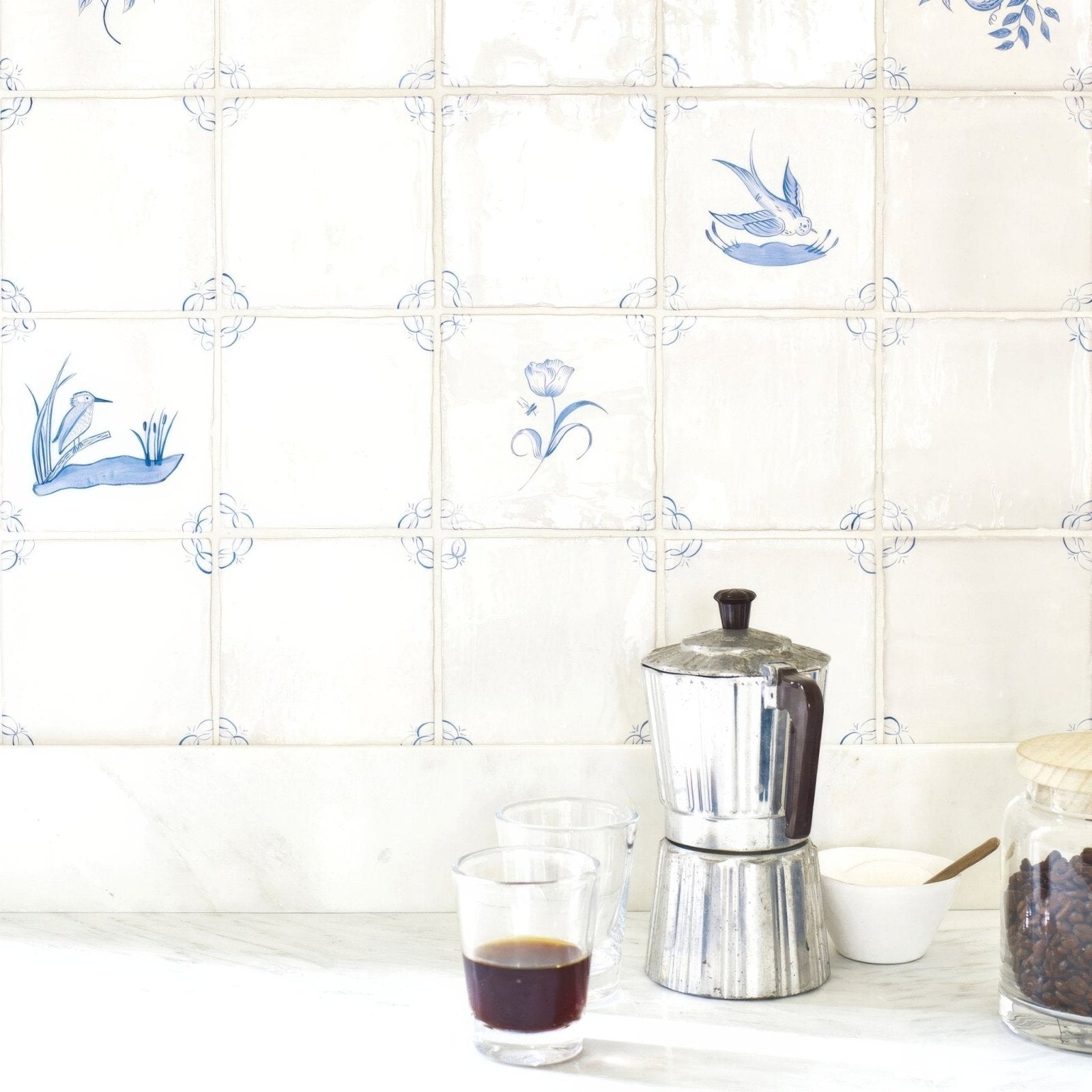 Silver metallic moka pot with dark brown handle and lid next to english delft blue gloss corner tile