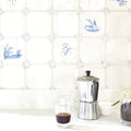 Silver metallic moka pot with dark brown handle and lid next to english delft blue gloss corner tile
