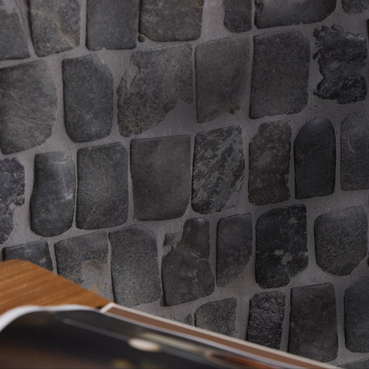 Dark gray irregularly shaped stone tiles with rough texture form enso cobble mosaic strip charcoal wall panel