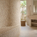 Curved wall and bench clad in light beige irregular stone mosaic tiles of enso cobble mosaic strip sand design