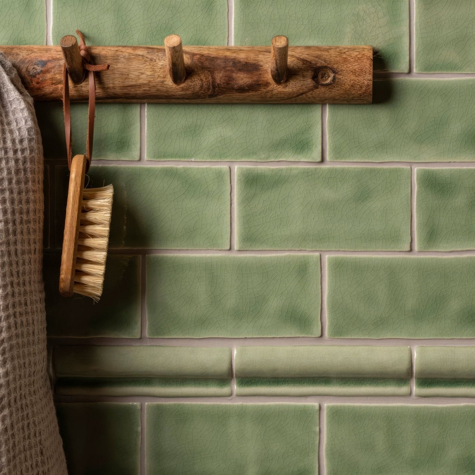 Half tile estuary green tiled wall with a rustic wooden hook rack featuring three natural toned pegs mounted
