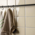 Beige waffle-weave cotton towel with fringed edges hanging from black hook in fennel field tile pattern