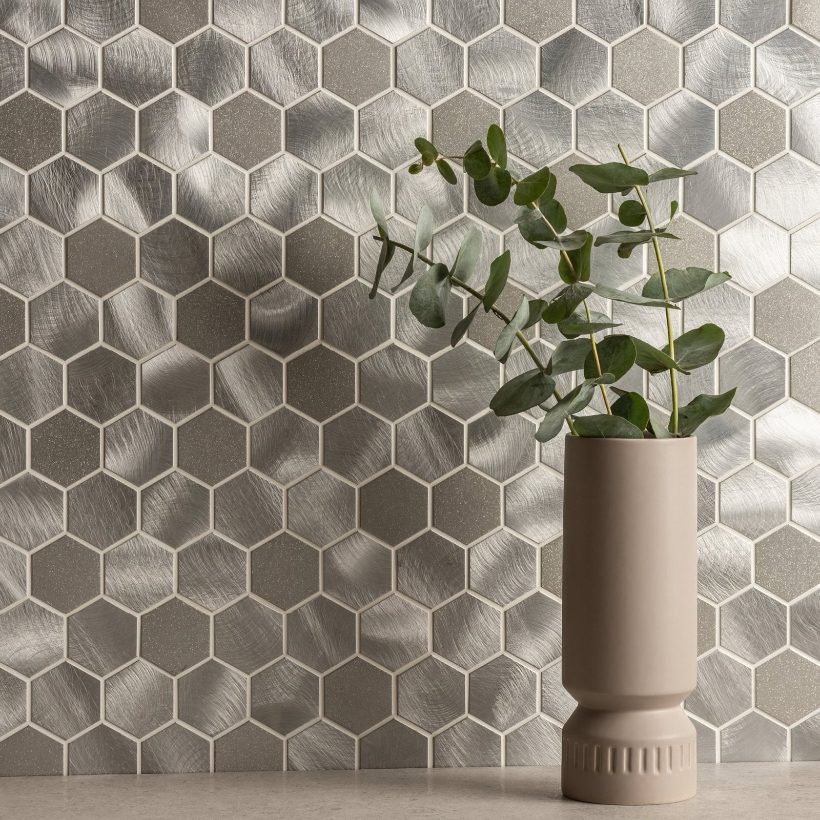 Beige ceramic vase with ribbed base holding eucalyptus branches in fenrir silver mixed finish hexagon mosaic design