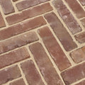 Reddish-brown flanders warm russet tumbled clay pavers with textured surface laid in a herringbone pattern with beige mortar