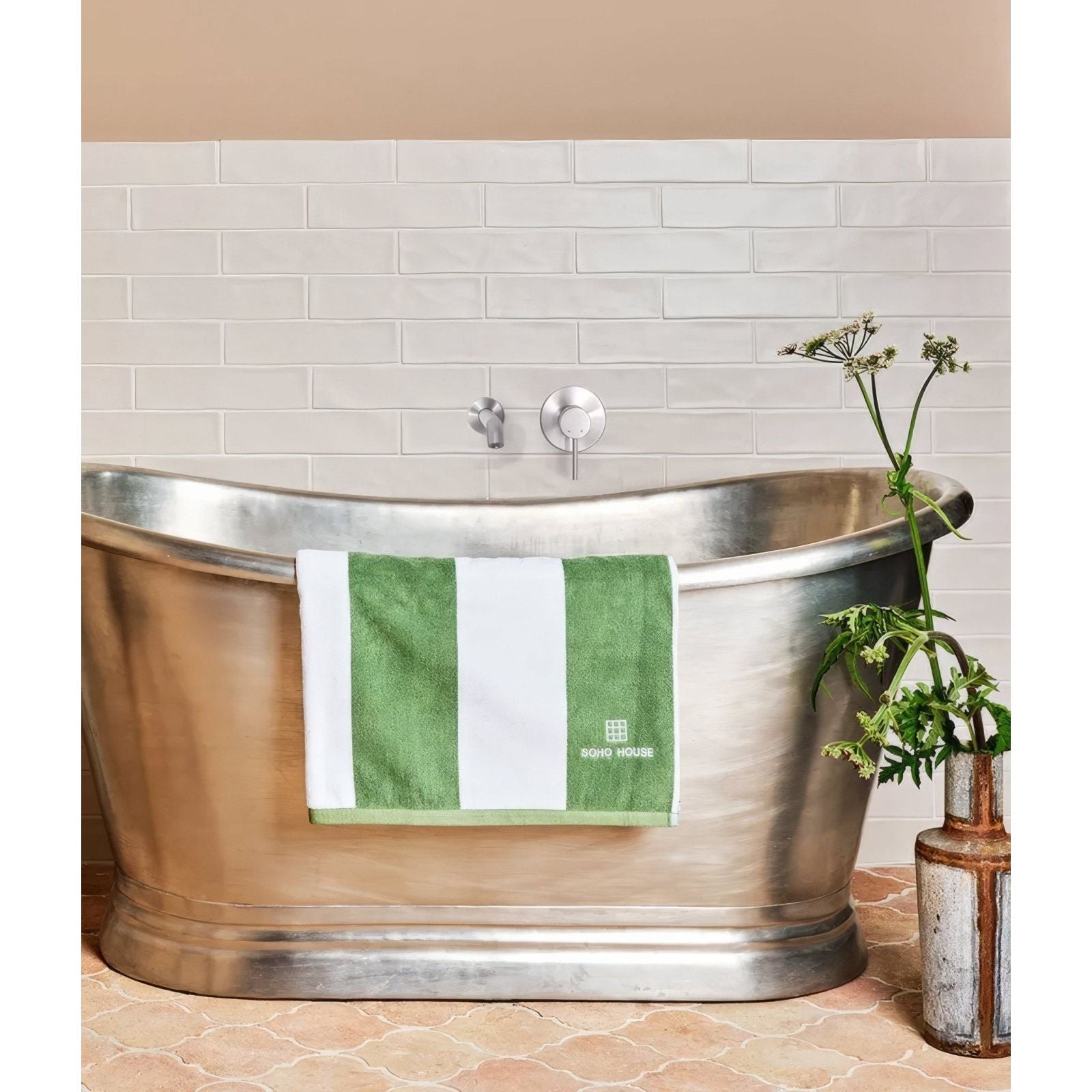 Green and white striped fondant ceramic ecru towel with subtle embroidered logo hanging over metallic bathtub