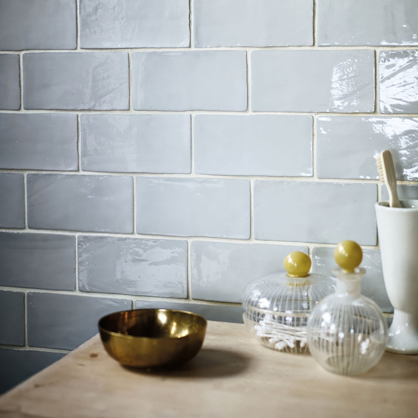 A small metallic gold bowl with a smooth reflective surface on a wooden countertop showcasing forecast cromarty rectangle glazed tile