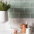 A white ceramic hanging planter with sleek modern design holding lush green herbs featured in forecast sky square glazed tile