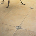 Square metallic inlay with raised floral design set into beige stone tiles from foundry lotus inset series
