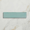 A rectangular teal porcelain tile with a matte finish from foundry resting on a white marble surface