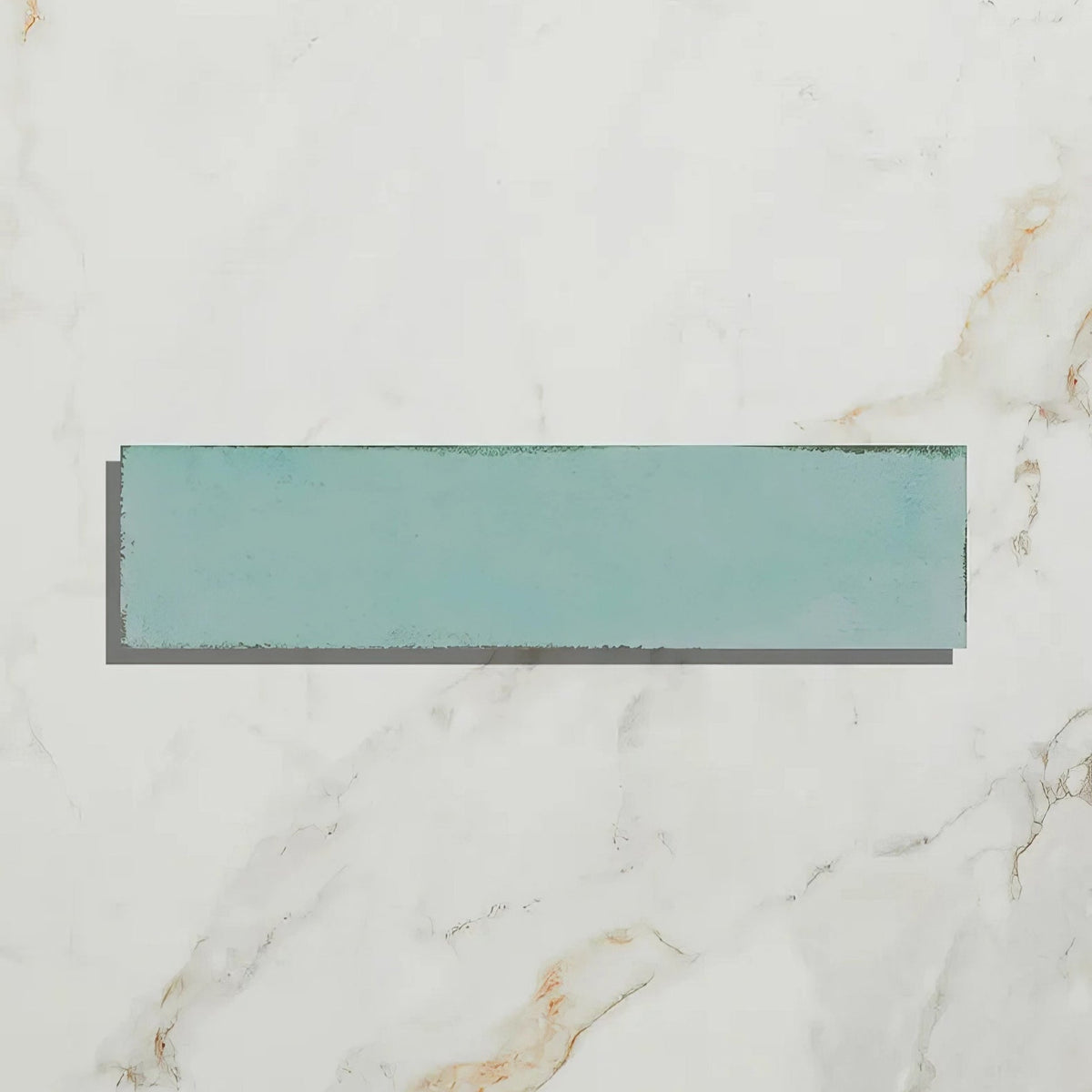 A rectangular teal porcelain tile with a matte finish from foundry resting on a white marble surface