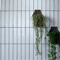 Foundry Porcelain Bianco white porcelain subway tiles with dark metal wall planters and greenery
