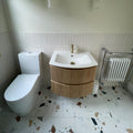 Modern white ceramic sink with gold faucet on floating wooden vanity with vertical grooves and two drawers shown with frammento multi terrazzo effect porcelain tile