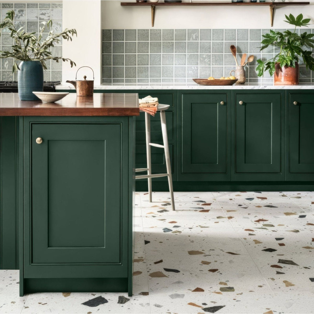 Deep green shaker-style kitchen cabinets with raised panel doors and round brass knobs featuring frammento multi terrazzo effect porcelain tile