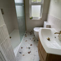 White ceramic sink with gold-toned faucet and stopper on wooden vanity featuring frammento multi terrazzo effect porcelain tile