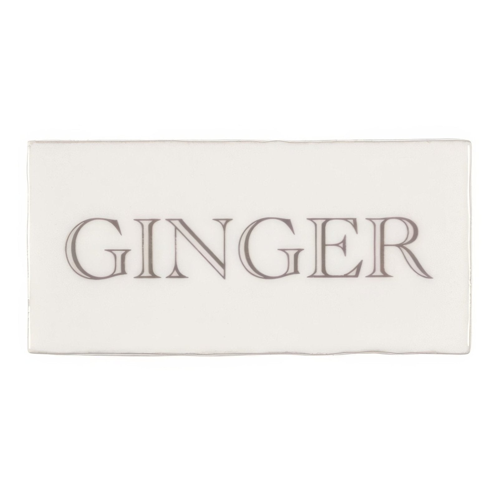 Cream-colored rectangular ginger soap bar with embossed dark gray serif font on a grey cotton background