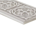A rectangular off-white ceramic giralda niebla grey border tile with raised floral and leaf patterns