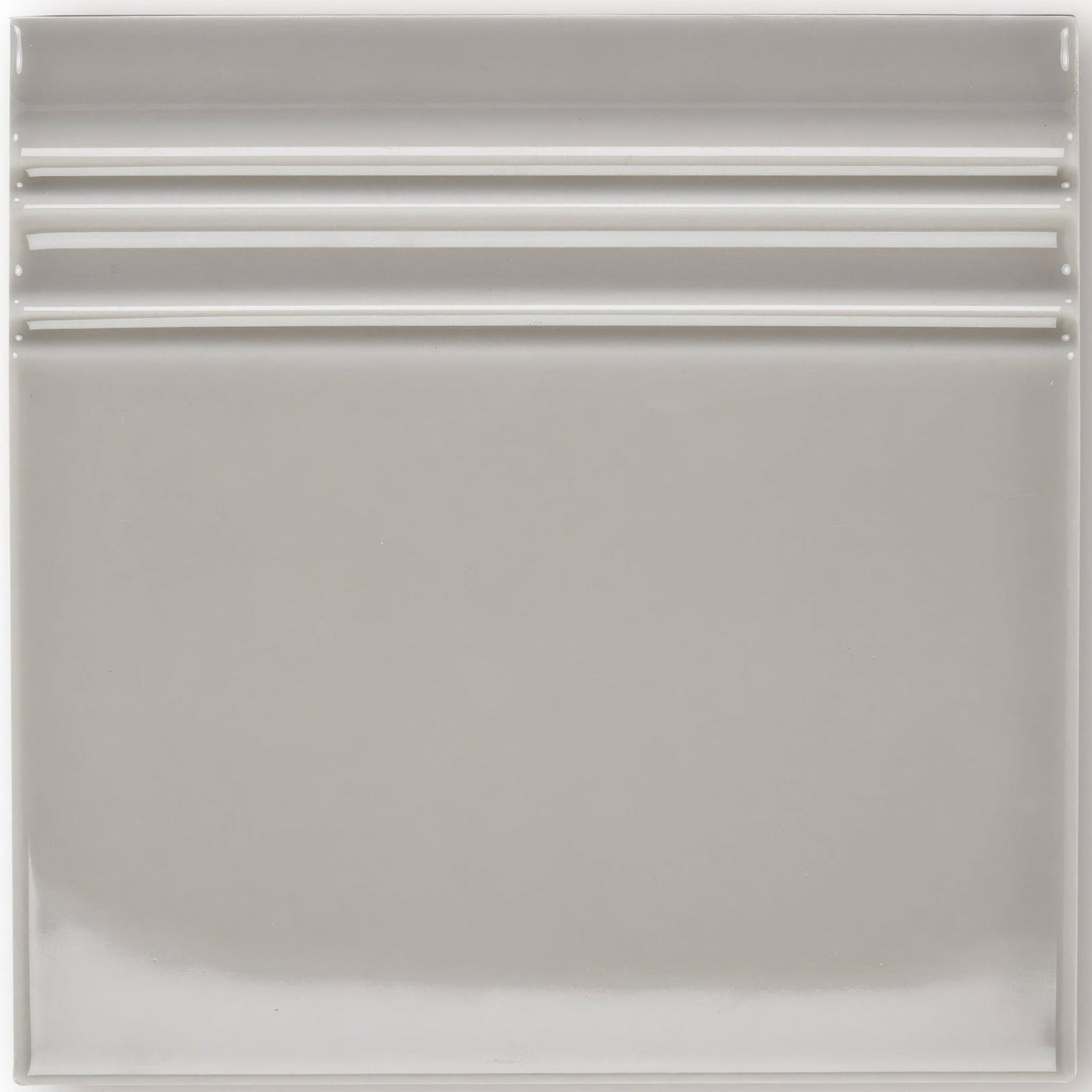A sleek square ceramic giralda niebla grey skirting tile with a smooth glossy finish and three horizontal ridges near the top