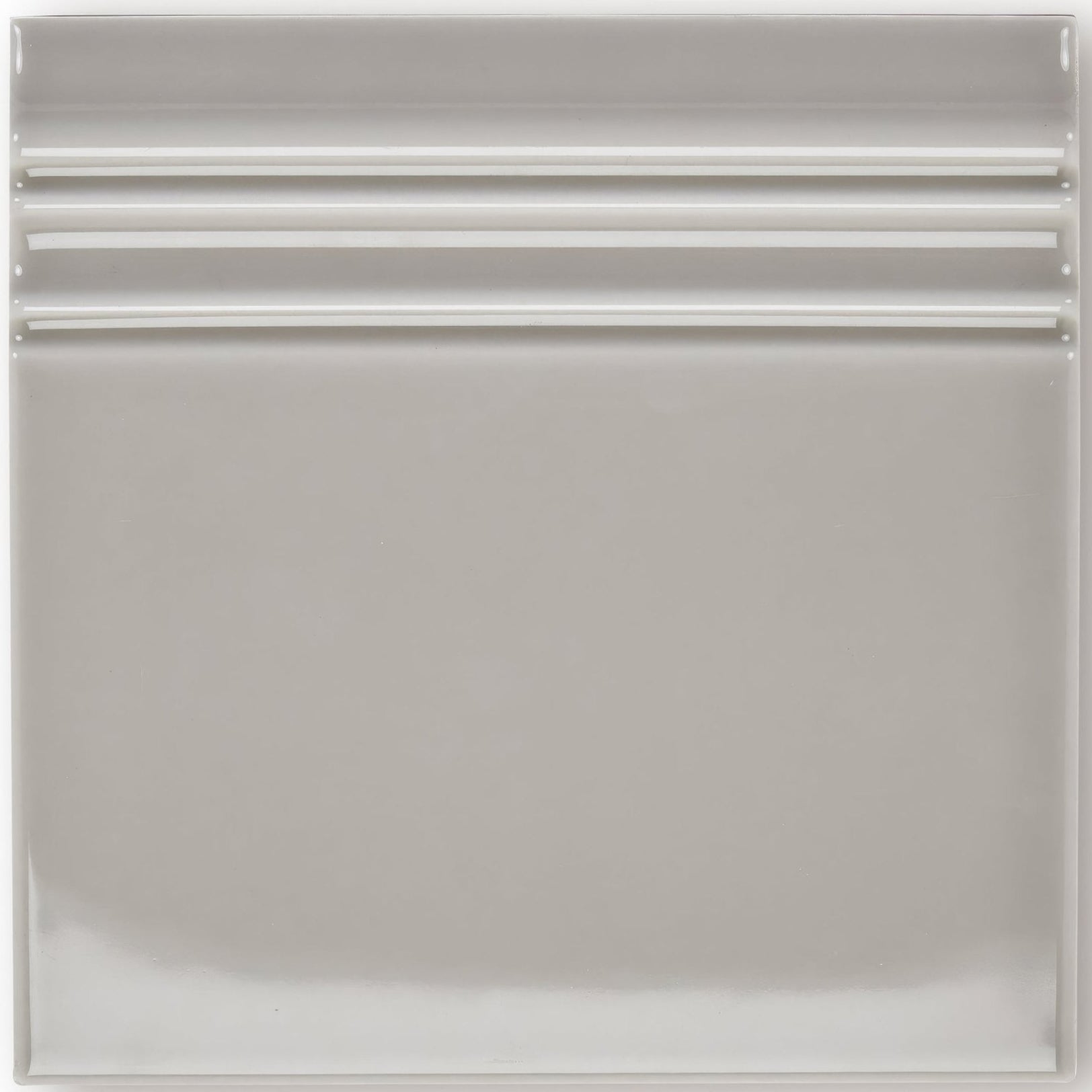 A sleek square ceramic giralda niebla grey skirting tile with a smooth glossy finish and three horizontal ridges near the top