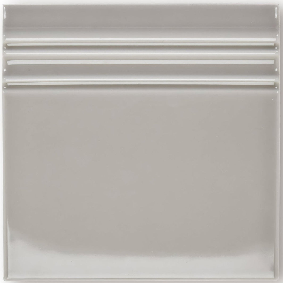 A sleek square ceramic giralda niebla grey skirting tile with a smooth glossy finish and three horizontal ridges near the top