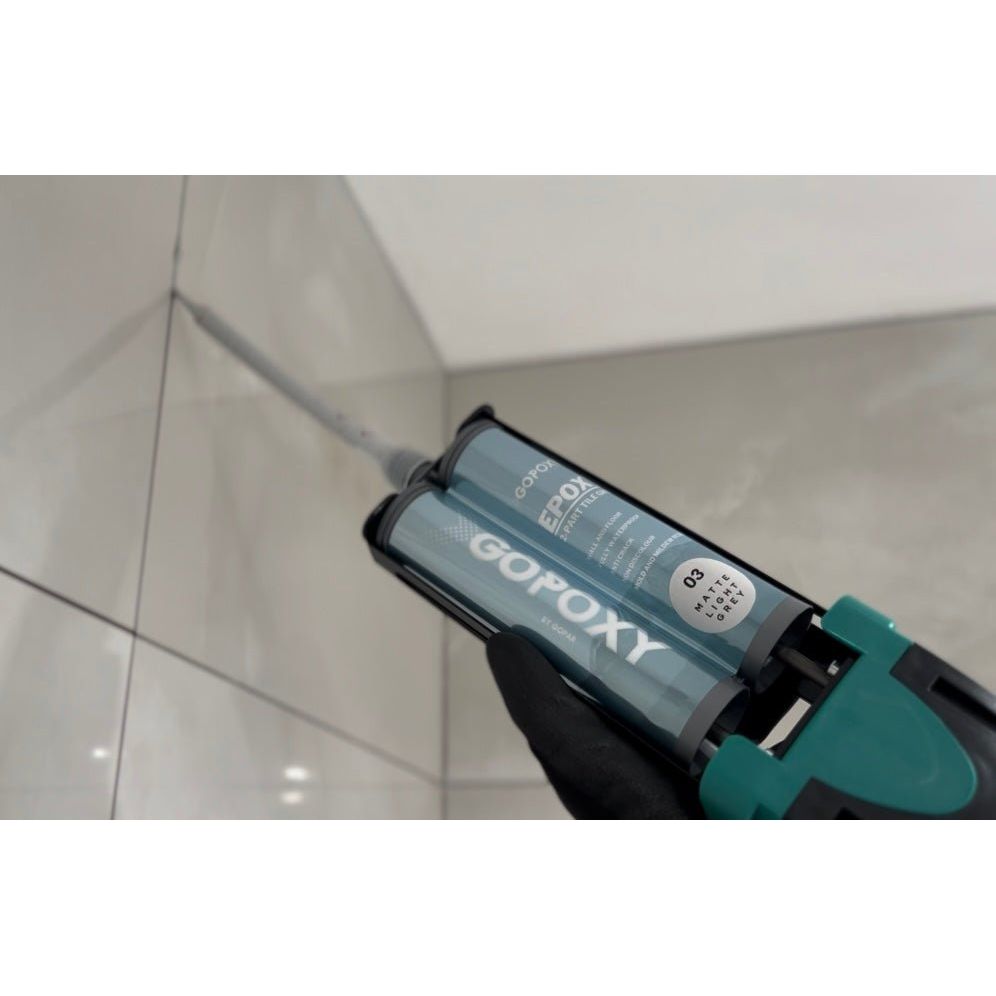 A teal and black gopoxy epoxy adhesive gun applying gray sealant to tile grout for epoxy grout restoration