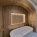 Gold-hued gravity aluminium trace gold mosaic tile wall with built-in illuminated mirror and freestanding white bathtub