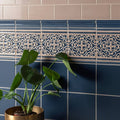 A potted plant with broad glossy green leaves in a gold pot against grosvenor palladian beige on ascot blue tiles