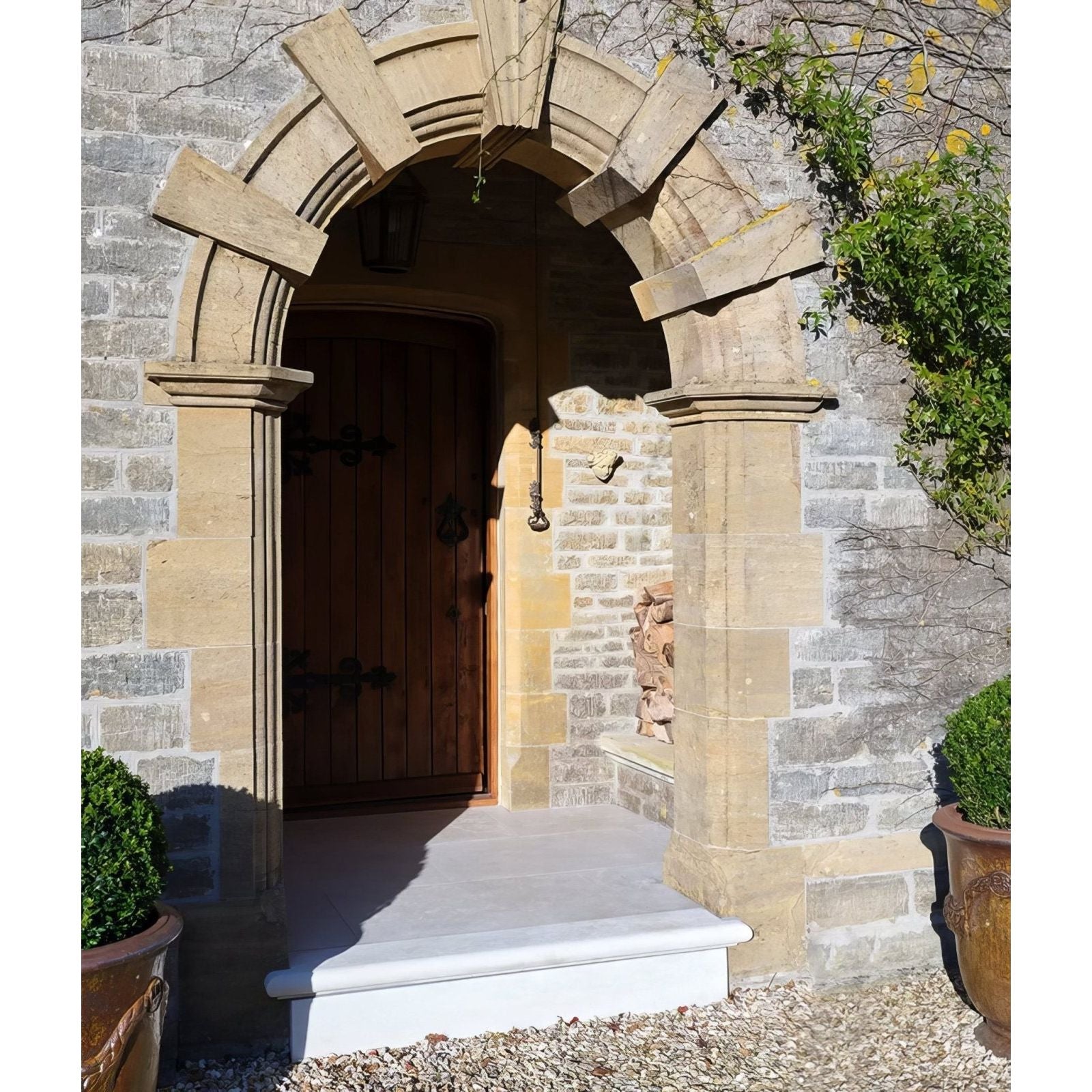 The wychwood limestone velvet finish features an arched limestone doorway with a golden brown wooden door and dark hardware