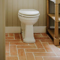 White ceramic toilet with closed lid against beige panelled walls and handmade classic terracotta rectangle tile 10x30cm flooring