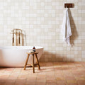 White freestanding bathtub with gold-toned faucet and fixtures alongside handmade classic terracotta square tile 20 x 20 cm