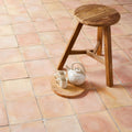 A rustic wooden stool with a round slatted seat and three angled legs beside handmade classic terracotta square tile 30.5x30.5cm