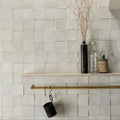Tile wall with a shelf holding decorative items and a cup with a hook.