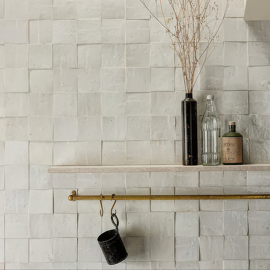 Tile wall with a shelf holding decorative items and a cup with a hook.