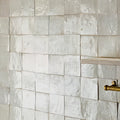 Close-up of a tiled shower wall with a gold fixture.