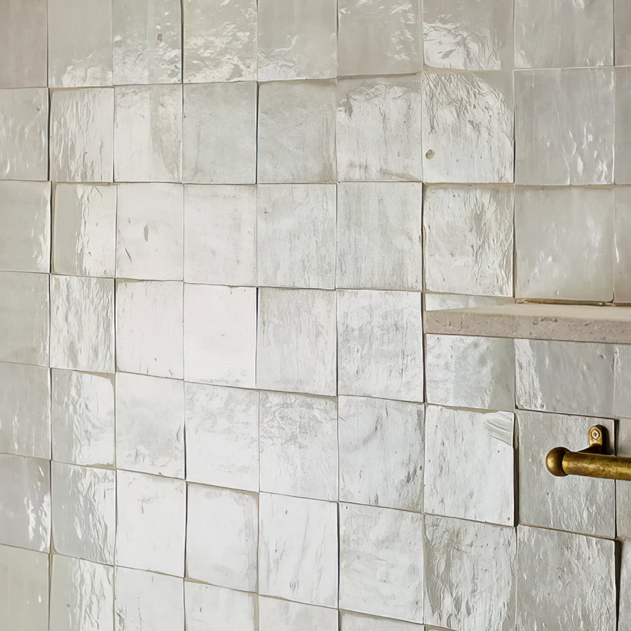 Close-up of a tiled shower wall with a gold fixture.