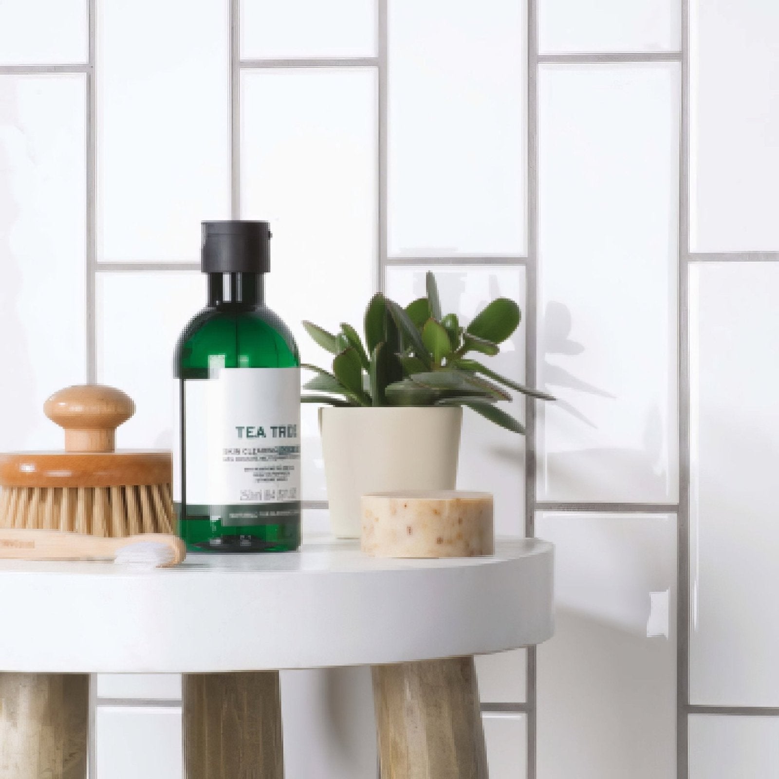 Green glass tea tree bottle with black cap and white label in brick tile helmingham product image
