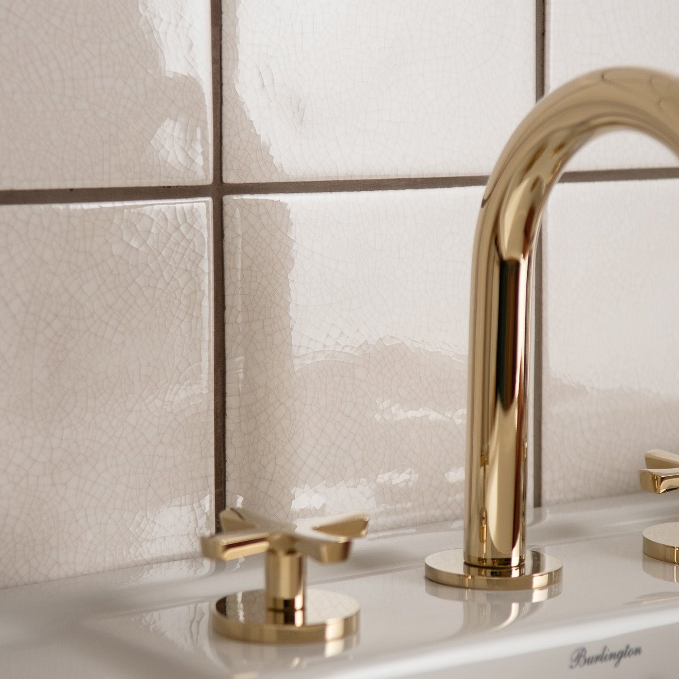 Gold-toned sleek modern faucet with curved spout and cross-handle knobs featured with helmingham crackle field tile