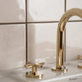 Gold-toned sleek modern faucet with curved spout and cross-handle knobs featured with helmingham crackle field tile
