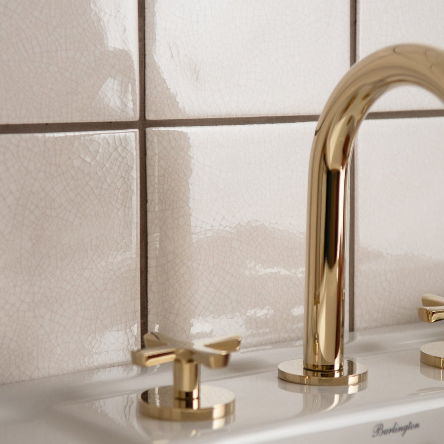 Gold-toned sleek modern faucet with curved spout and cross-handle knobs featured with helmingham crackle field tile