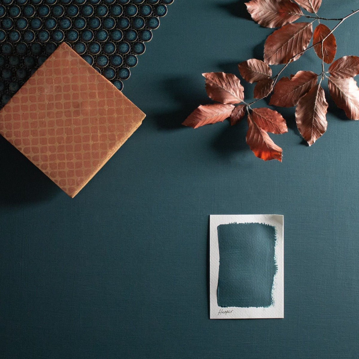 A square sample of deep teal paint hopper rests on a dark green surface in the hesper product line