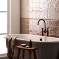 White freestanding bathtub with black faucet and handles against textured taupe tiles featuring hessian torus moulding