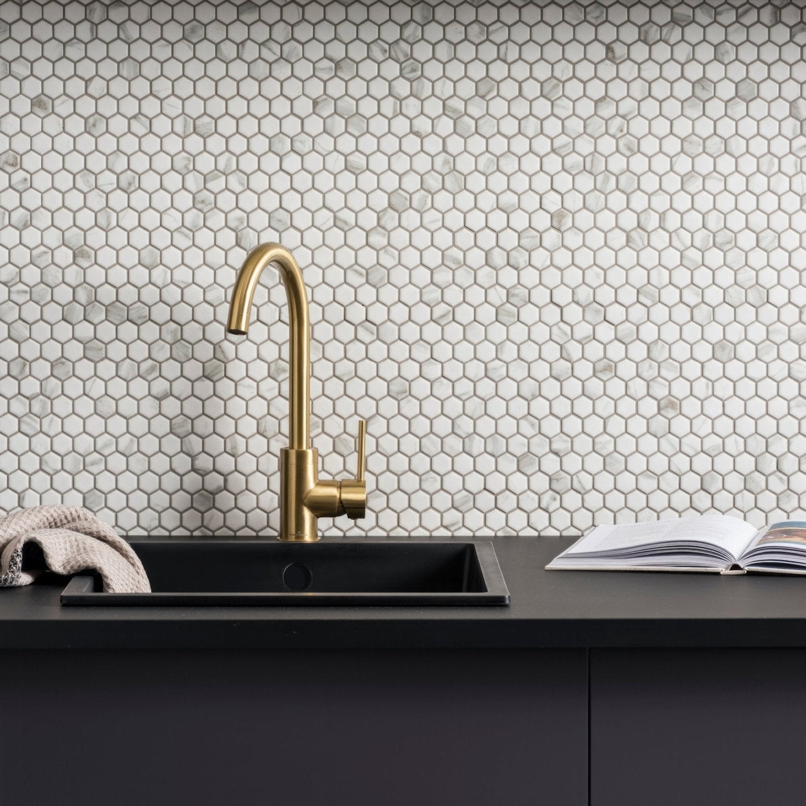 Gold-toned kitchen faucet with sleek curved spout and minimalist design paired with hexagon matt carrara white surface